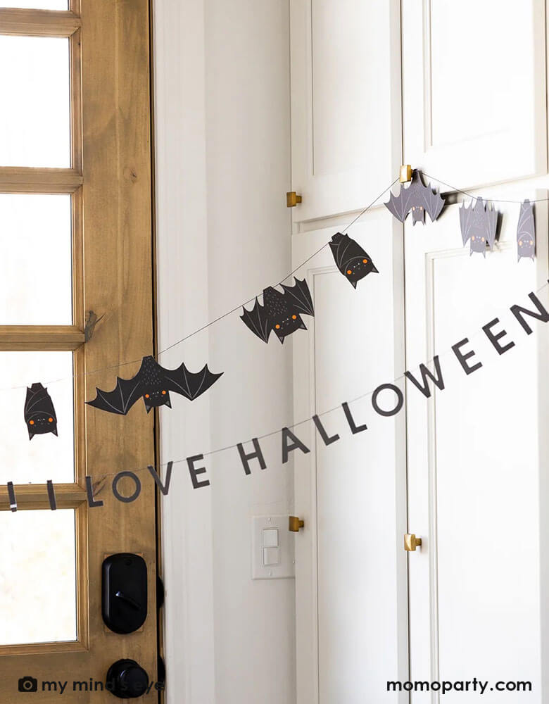 A door entrance decorated with Momo Party's 6' Freakin' Bats Garland by My Mind's Eye. This banner set includes a spooky stitched bat banner and a stitched word banner featuring the phrase "It's freakin bats! I love Halloween." These banners create a frightfully fun scene and sure to drive your guests batty this Halloween.