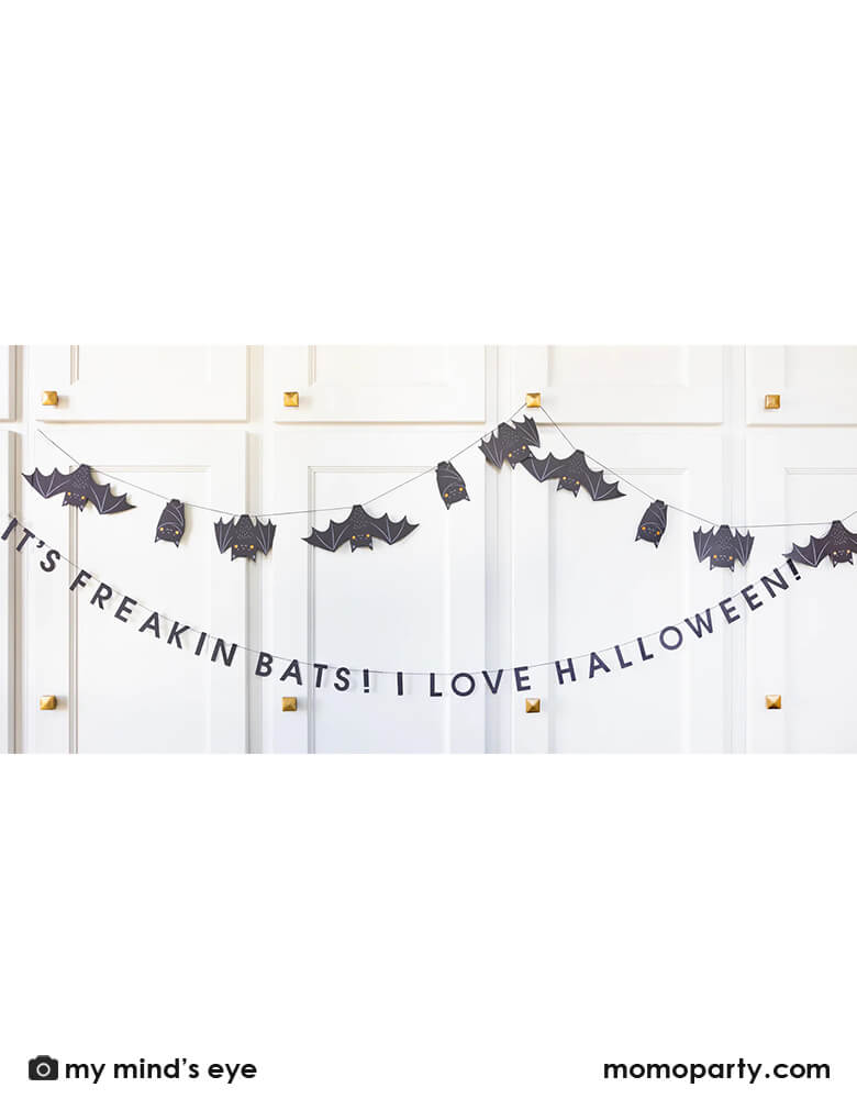 A white cabinet set decorated with Momo Party's 6' Freakin' Bats Garland by My Mind's Eye. This banner set includes a spooky stitched bat banner and a stitched word banner featuring the phrase "It's freakin bats! I love Halloween." These banners create a frightfully fun scene and sure to drive your guests batty this Halloween.