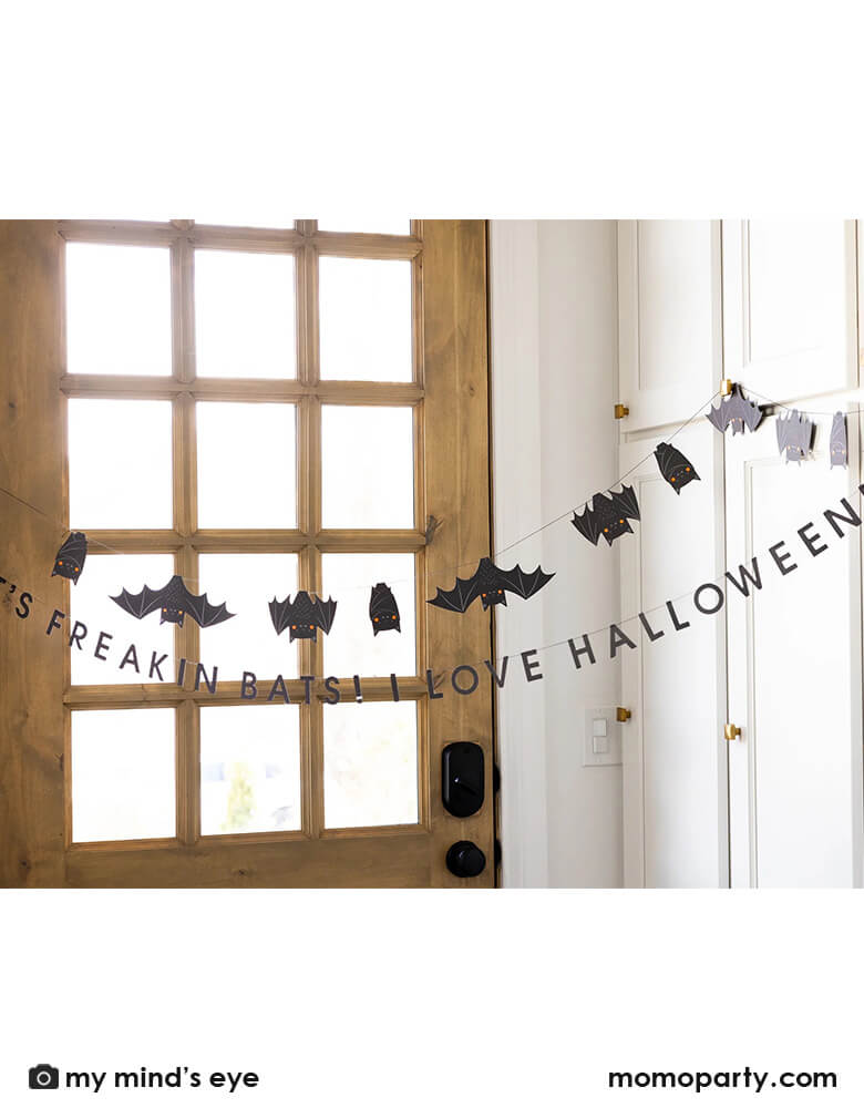 A door entrance decorated with Momo Party's 6' Freakin' Bats Garland by My Mind's Eye. This banner set includes a spooky stitched bat banner and a stitched word banner featuring the phrase "It's freakin bats! I love Halloween." These banners create a frightfully fun scene and sure to drive your guests batty this Halloween.