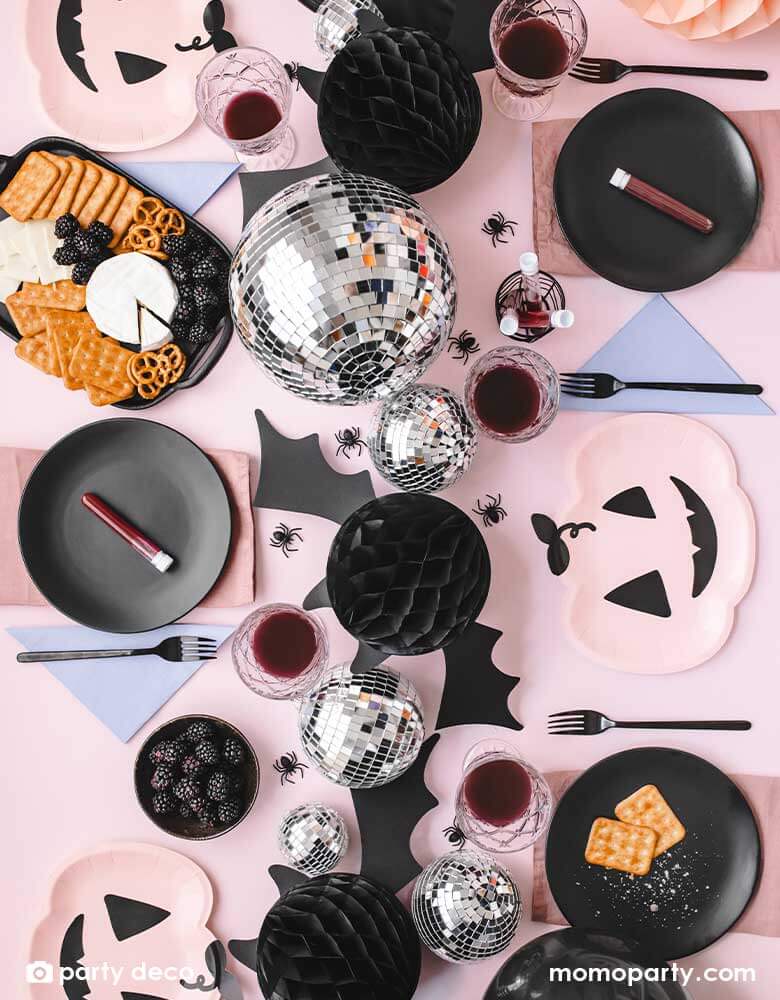 A pink Halloween party table featuring Momo Party's pink Halloween party supplies including pink pumpkin shaped plates, lilac napkins and onyx black round plates as the tableware. In the middle, there are Momo Party's 5.8" bat honeycombs and disco balls as the table centerpiece. There's also some spider confetti spread throughout the pink table, makes it a spooky yet adorable tablescape inspiration for a kid-friendly Halloween party.