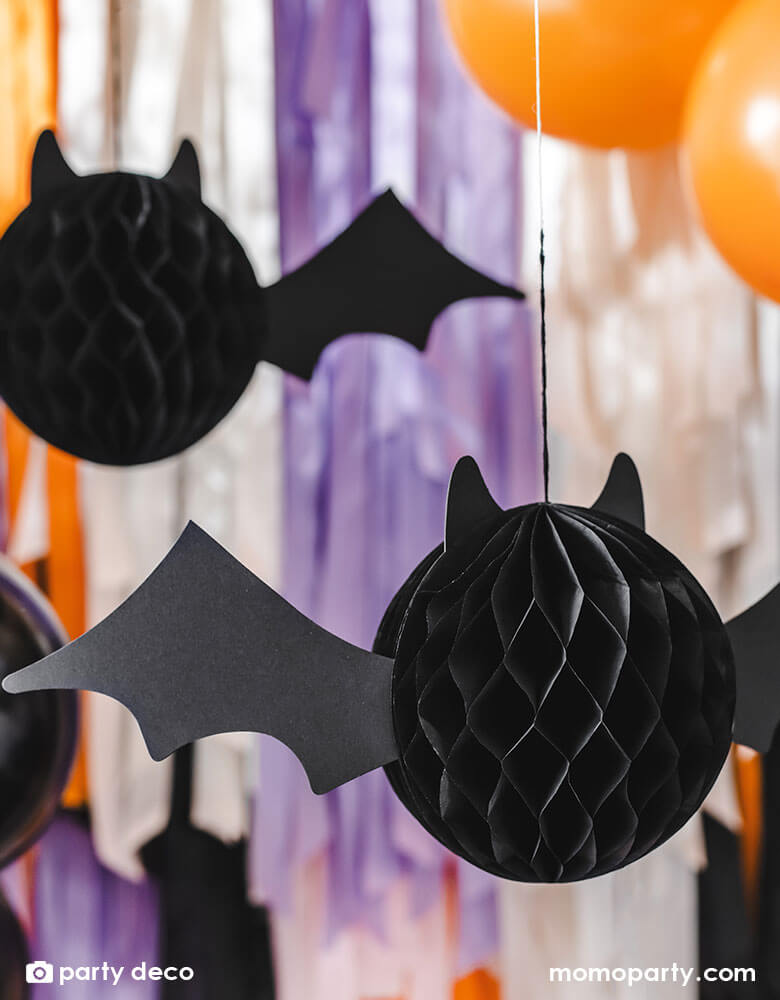 Momo Party's 5.8" bat honeycomb hanging decoration by Party Deco in front of a colorful fringe wall backdrop in the color of lilac, white, orange and black, makes it a great party inspiration of decorations for a kid-friendly Halloween bash.