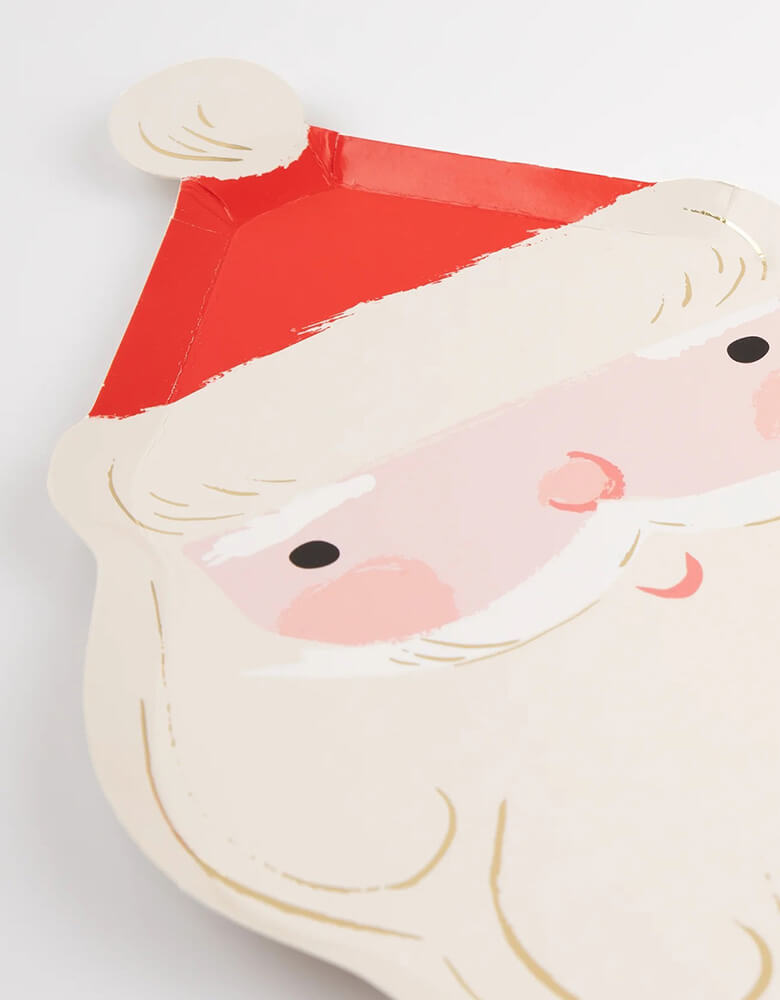 A close up shot of Momo Party's 7.25 x 11.5 inches Jolly Santa shaped plates by Meri Meri. For a festive party table guaranteed to delight your guests smile, look no further than these Santa plates. It doesn't get more traditional than this jolly fellow, and the red and gold colors will team beautifully with all your Christmas tableware.
