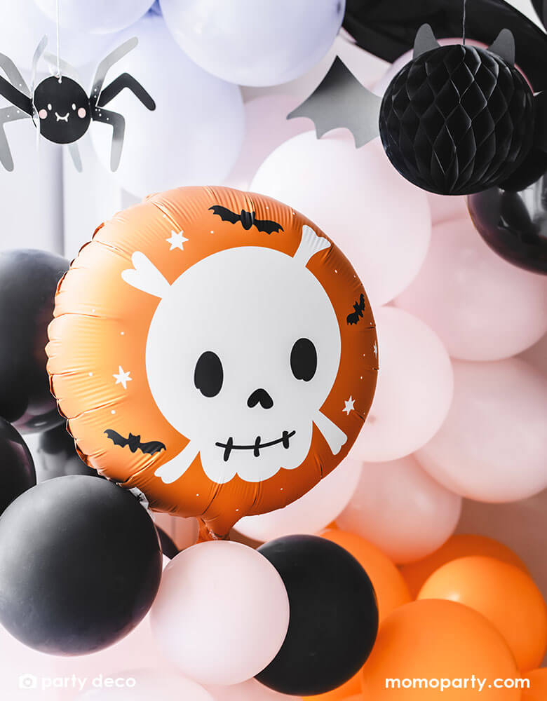 A festive Halloween party balloon set up featuring Momo Party's 14" orange round skull foil balloon by Party Deco. A festive orange skull with cute details is the perfect addition to a not-so-spooky kid's Halloween party! In the back of the skull foil balloon there is a balloon garland in black, orange, pink and purple colors, around the balloon garland, some paper spider and bat honeycomb decorations are topped to create a spooky yet adorable vibe to a fun kid's Halloween bash.