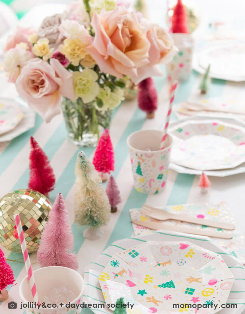A festive Christmas tableset featuring Momo Party's Merry and Bright tableware collection by Daydream Society. The Christmas themed plates, cups, and napkins on a mint striped table cover which adorned with bottle brush Christmas trees in different shades of pink and a gold disco ball. With the floral centerpiece, it makes a great inspo for a festive party table setting this Holiday season.