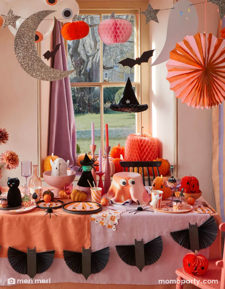 An adorable pink Halloween party setup by Meri Meri featuring Momo Party's pink orange striped pumpkin plates, napkins, honeycomb pumpkins as centerpiece and pastel halloween honeycomb garland featuring bats, witch hats, pumpkins hanging from the ceiling, all makes a perfect inspiration for kid's pink themed Halloween party!