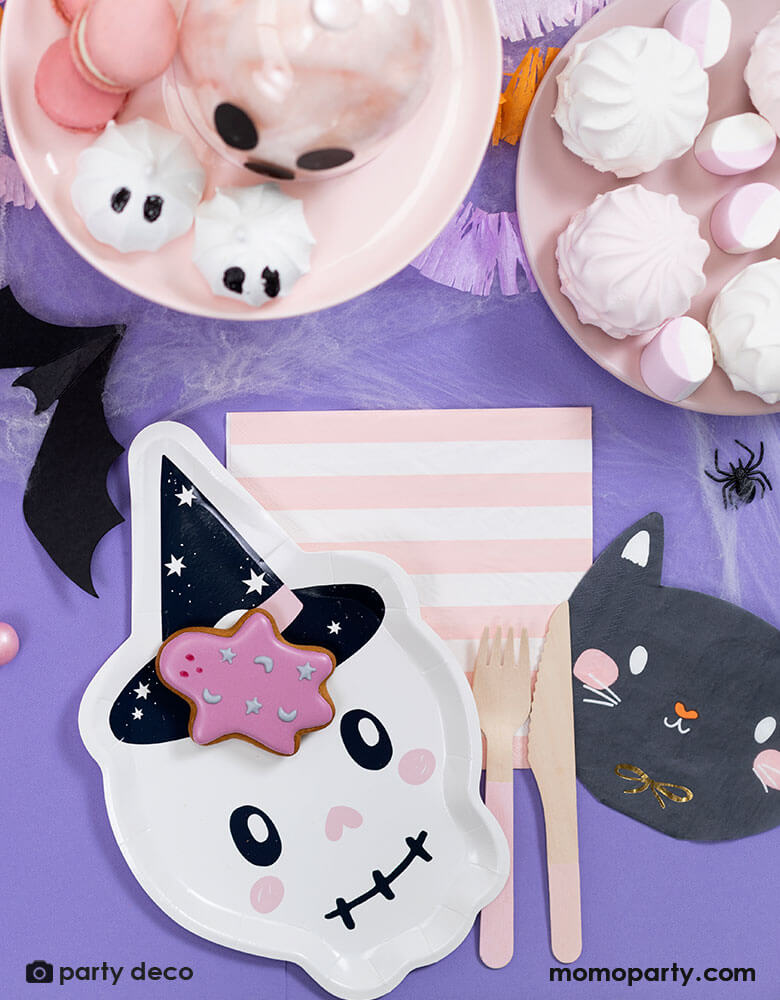 A purple Halloween party table featuring 7" x 10.6" pink skull shaped plate and black cat shaped napkin and pink striped napkin from Momo Party. Around the tableware there are some pink Halloween themed treats including marsh mellows, macaroons, cotton candies, with bat and spider confetti scattered around the table, it makes a great inspiration for a kid-friendly Halloween party.