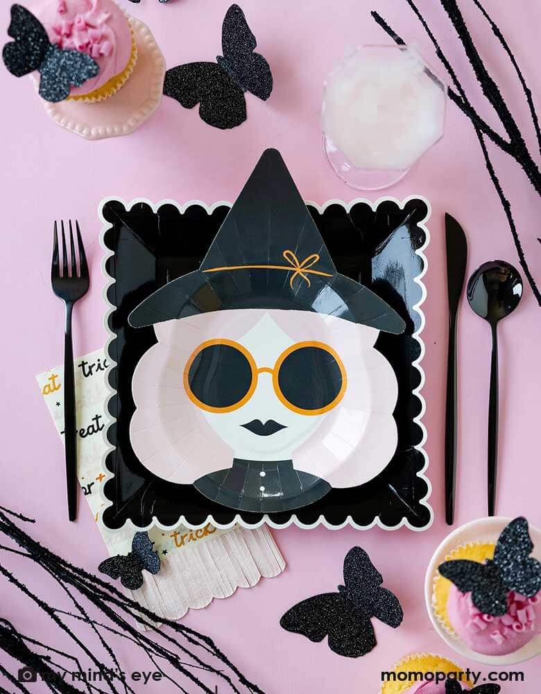 A pink Halloween table featuring Momo Party's 10" x 8" pink witch shaped plate, along with the black scallop edged plates, the pink trick or treat fringe napkins and the glittered butterfly decorations around the tableware, it makes a chic and stylish girly pink Halloween party idea and inspiration.