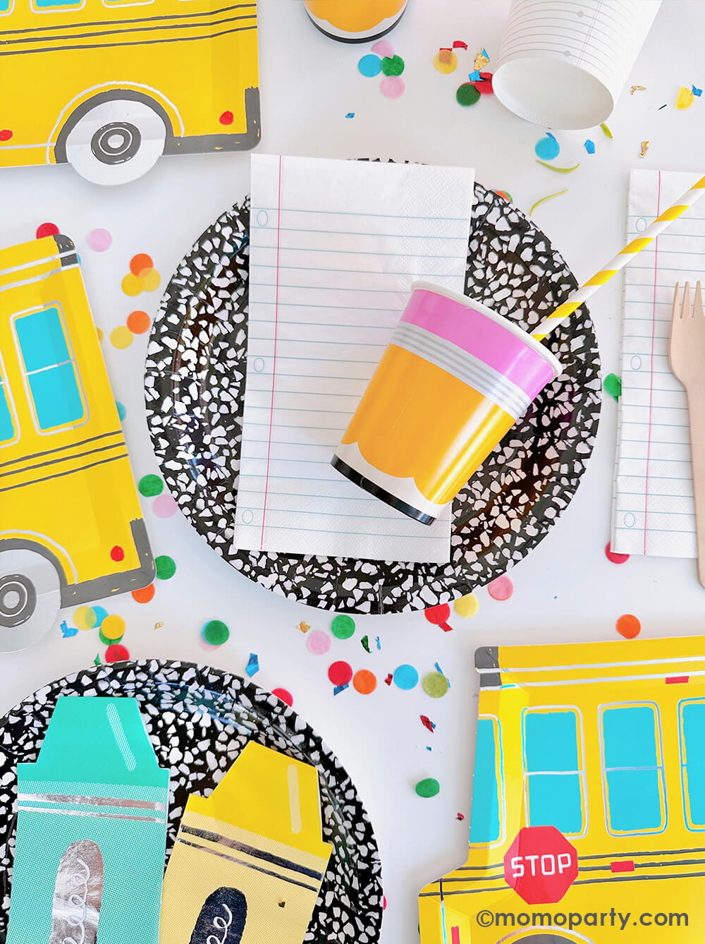 A colorful back to school party tablescape featuring Momo Party's back to school collection including notebook napkins, pencil party cups, school bus shaped plates, colorful crayon shaped napkins on the art book inspired round plates, makes a great inspiration for a school themed celebration including kid's back to school party or first day of school celebration.