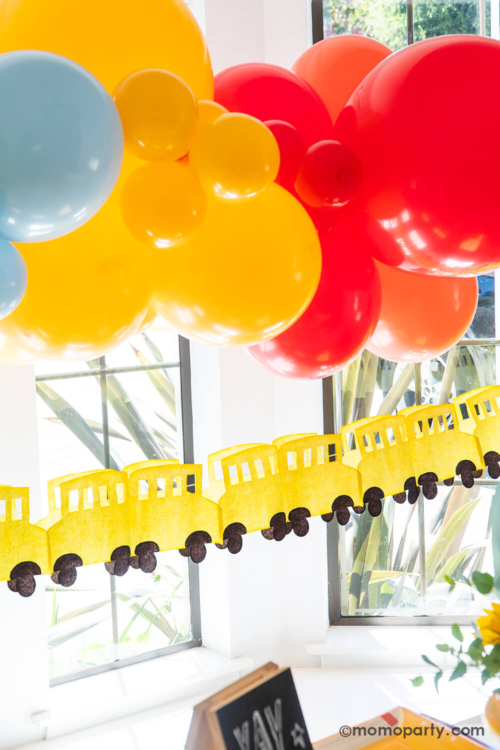 A festive back to school, first day of school party decoration featuring a colorful yet modern balloon arch of the classic school colors of red, yellow and blue, and the school bus paper garland from Momo Party. These decors are easy to put together and creates a wow factor to your child's school themed celebration, be it a back to school playdate party, a first day of school breakfast or a teacher appreciation event.