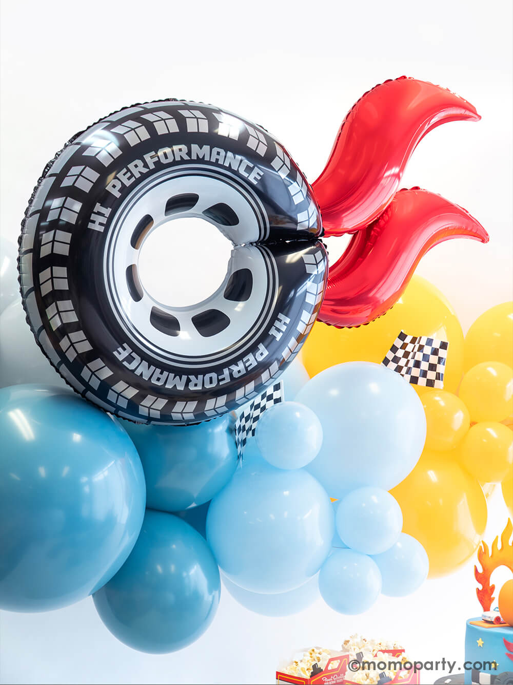 A close up of Momo Party's Hot Wheels themed balloon decoration featuring an organic balloon garland in orange and blue, and a wheel shaped foil balloon with red curve balloons attached as flame. On the balloon cloud there are some race car checkered flags adorned, making this a perfect decoration backdrop idea for kid's Hot Wheels themed race car birthday party.