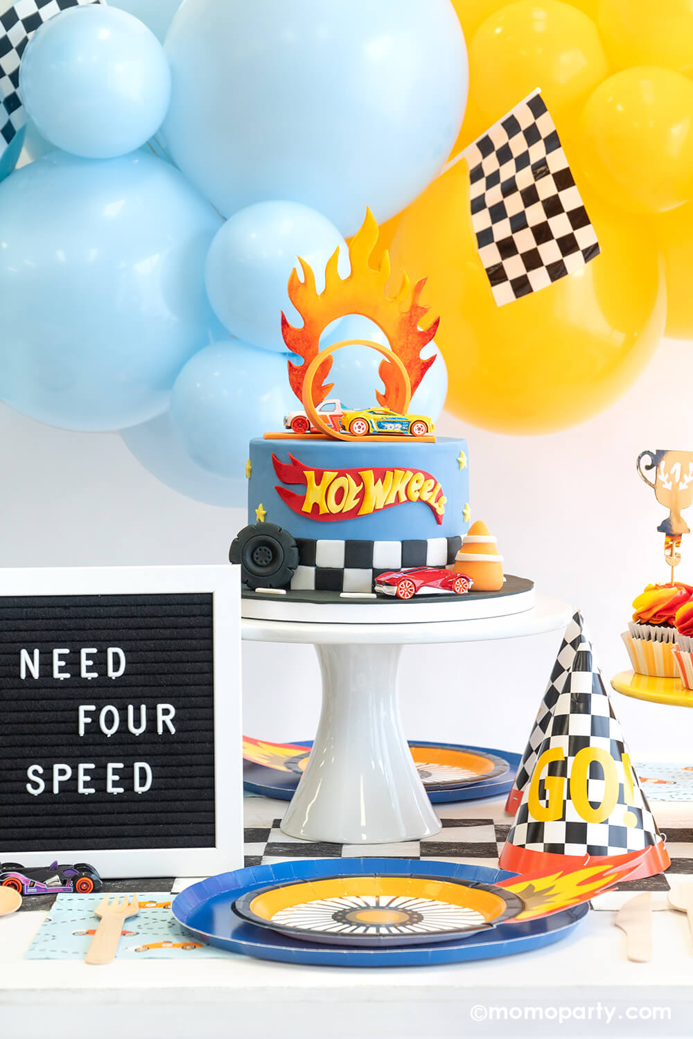 A "Need For Speed" boy's race car themed fourth birthday party featuring Hot Wheels balloon garland, Hot Wheels themed party supplies. A festive party table features Momo Party's Midnight Blue Dinner Plates, Wheel Shaped Plates, checkered party cups and checkered GO! birthday hats, with a Hot Wheels fondant birthday cake.