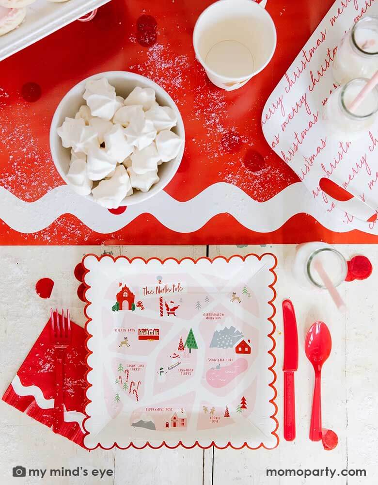 A festive Santa & Elf inspired red tablescape featuring Momo Party's Believe North Pole Map red scallop-edged 9" x 9" plates by My Mind's Eye, Elf inspired ric rac small fringe napkins, some milk bottles, and Santa face shaped party cups next to a red and white bamboo tray on ric rac red table runners, all makes a great inspo for a festive Holiday table setting.