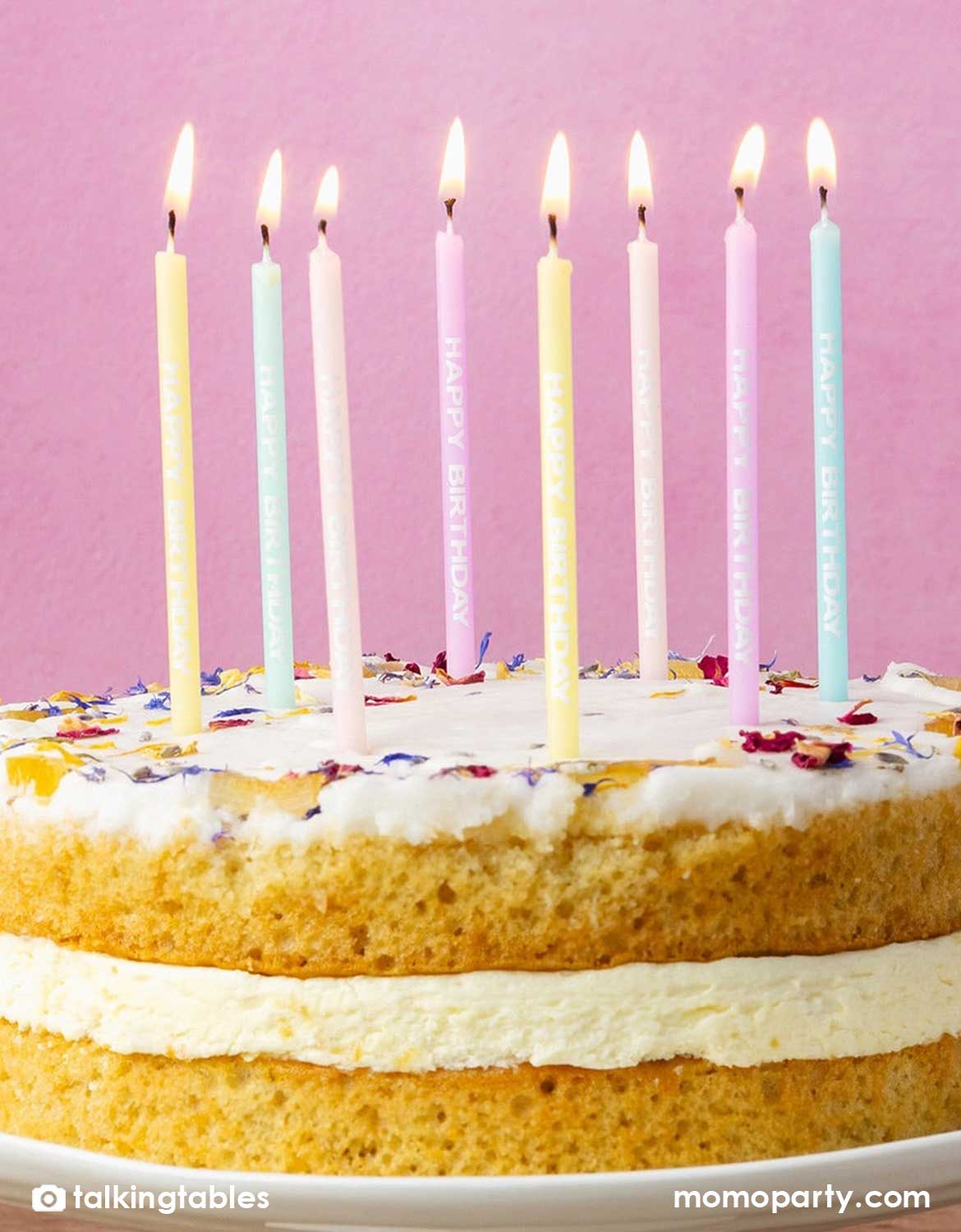 Momo Party's set of birthday candles with pastel Happy Birthday designs on a birthday cake decorated with flower pedals against a pink background.