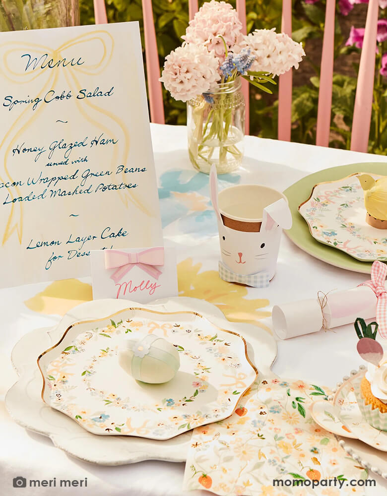 A spring Easter themed party table featuring Momo Party's Elegant Floral Party Collection including Meri Meri elegant floral Dinner and side plates, napkins and bunny shaped plates, on the table there are spring flowers, Easter inspired cupcakes, bunny shaped party cups and bunny shaped party crackers, and Pastel Bow Place Cards, makes this a perfect inspo for an elegant Easter celebration.