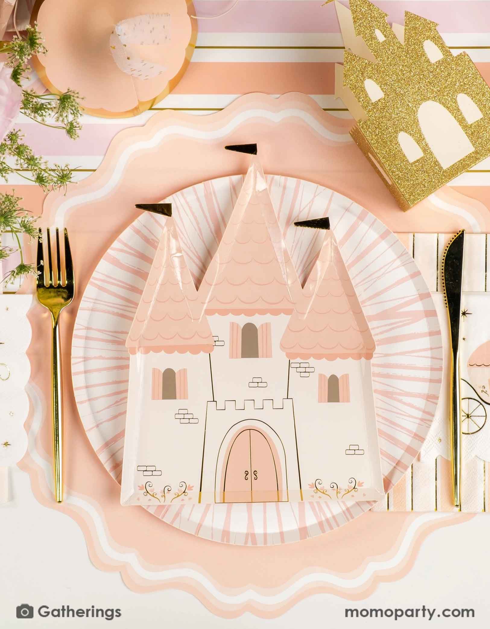 A beautiful princess themed tablescape with the Momo Party's castle shaped plate, princess carriage small napkin, gold cutlery, castle shaped treat box, a pastel pink birthday hat and the pink and gold striped table runner, with pink beautiful floral bouquet on the table, this creates a fairy tale tablescape for a girl's princess themed birthday party.