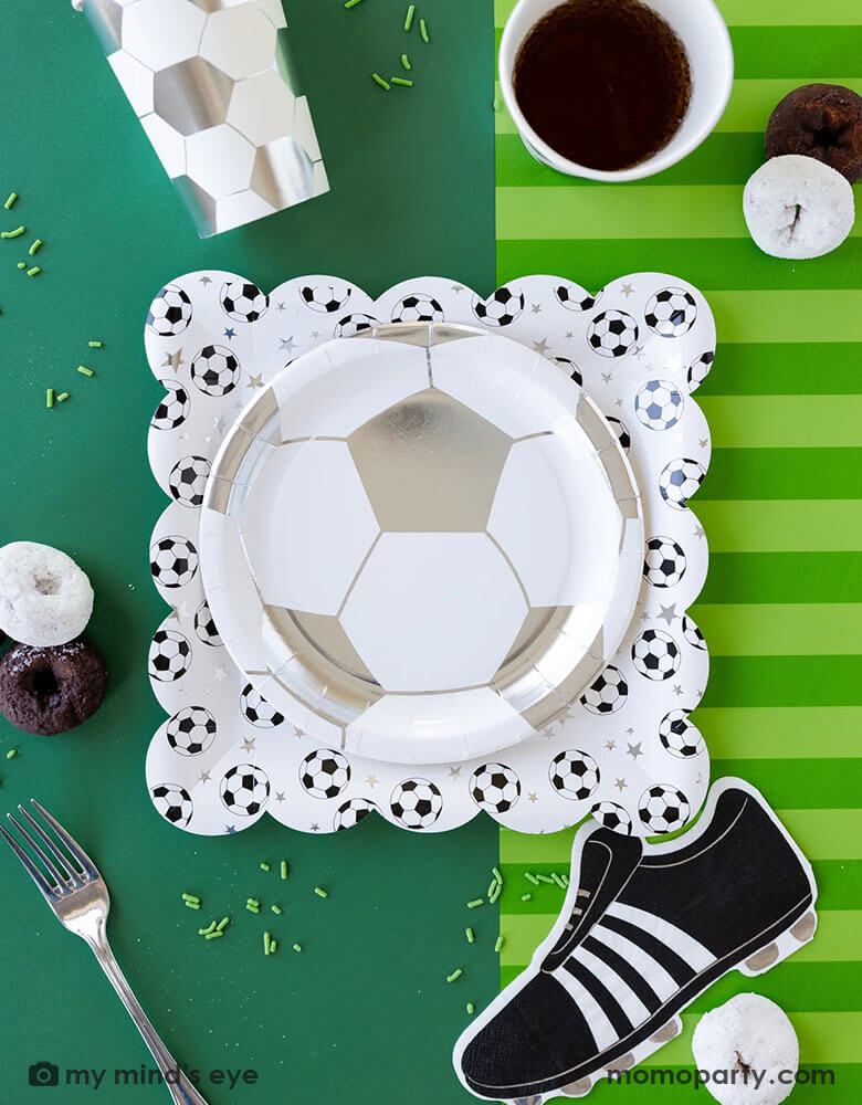 A fun soccer themed party table featuring Momo Party's soccer party collection including silver soccer shaped plates and party cups, cleat shaped napkins and soccer table runner by My Mind's Eye. With some snacks, green sprinkles around, this makes a great inspo for a fun kid's soccer themed birthday party or a championship celebration!