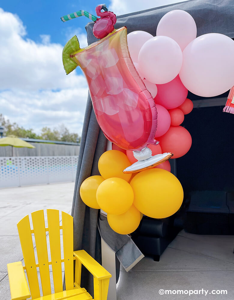 Summer Pool Party by Momo Party. Enjoy a poolside tent adorned with the 'Let's Flamingo Drink Foil Mylar Balloon' and coral, pink, goldenrod, and rose latex balloons. A bright yellow outdoor chair completes the vibrant summer vibe. Perfect for your summer bash!