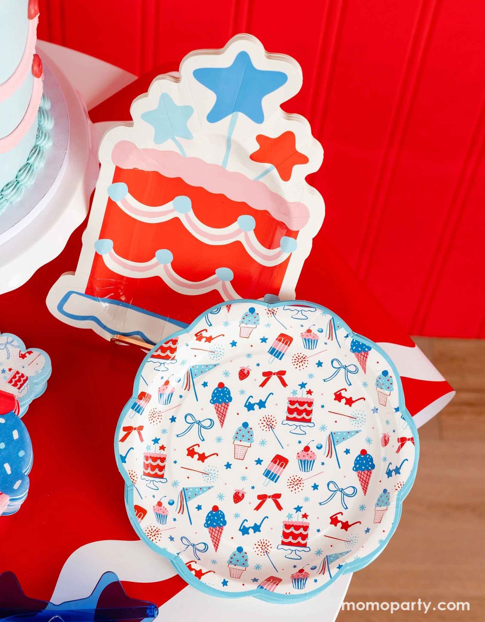 An overhead shot of a patriotic themed celebration featuring Momo Party's Summertime pattern plates, napkins, cake shaped paper plates, and ice cream shaped dinner napkins on a red paper table runner. The pattern features summer element icons in red, white and blue, perfect for a Fourth of July party, a Memorial Day BBQ or any patriotic summer celebrations!