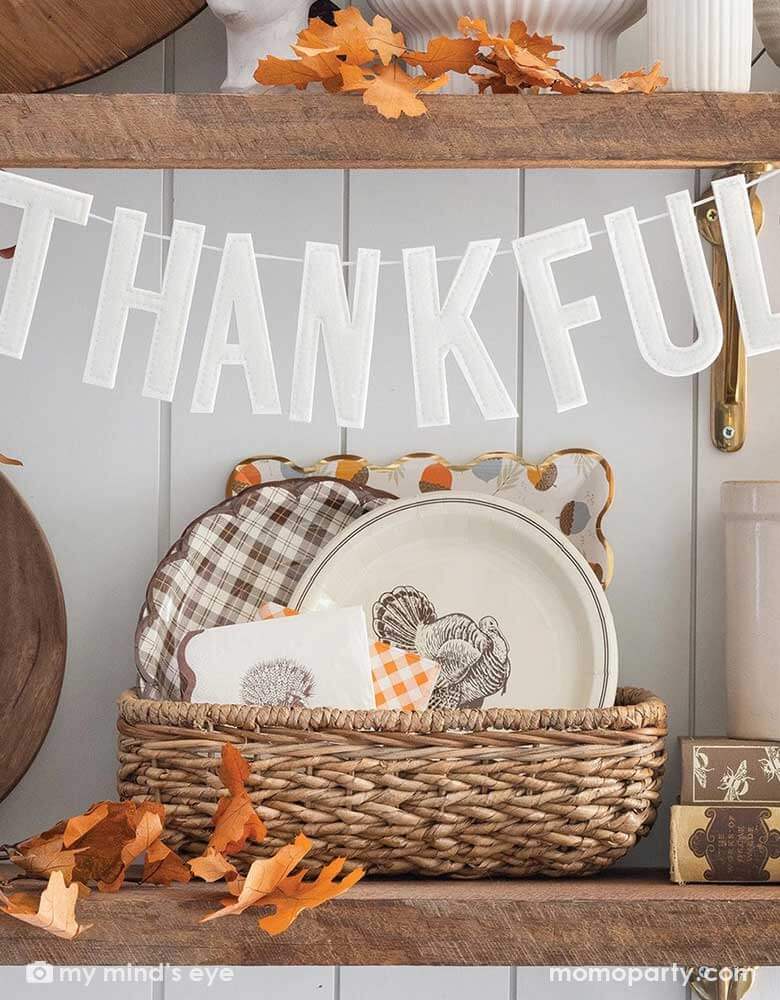 A kitchen shelf filled with fall themed tableware and decorations, on the self Momo Party's 3' "Thankful" puffy felt banner by My Mind'e Eye, which is hung across, makes it a perfect inspiration for fall home decor.