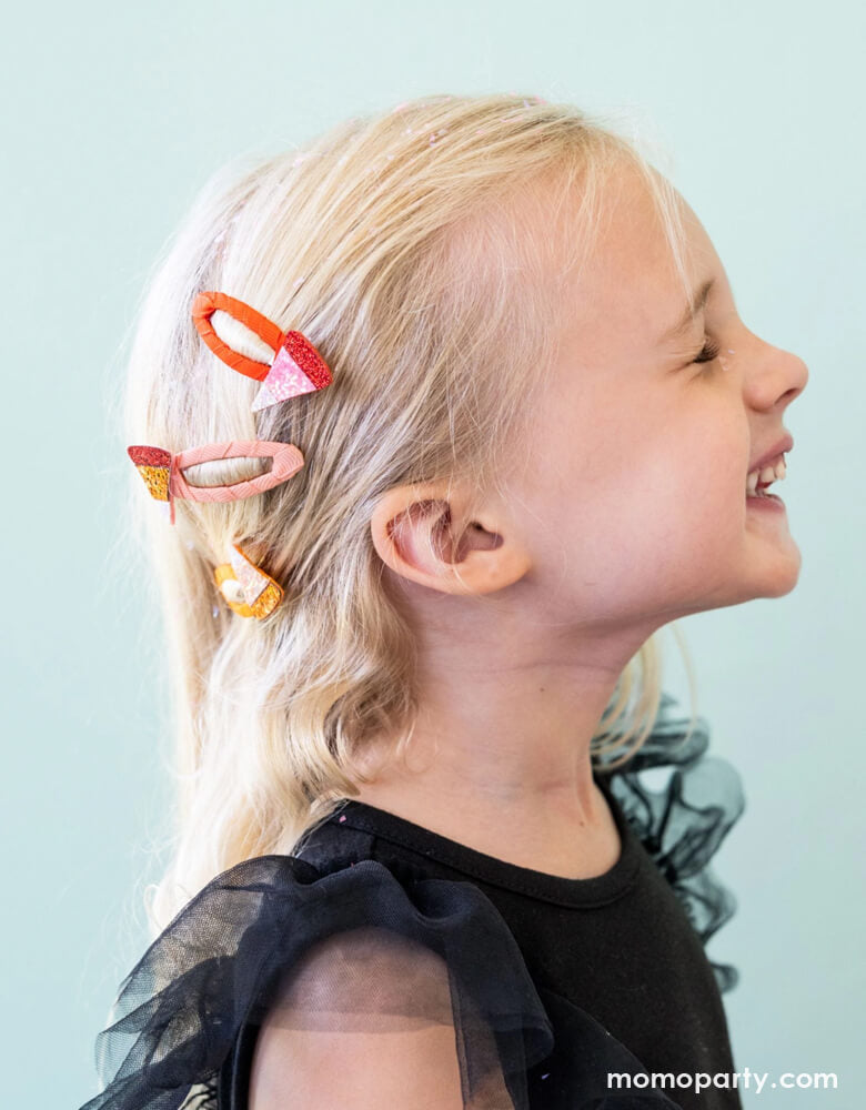 A girl in her Halloween costume with Momo Party's Halloween candy corn hair clips in a ponytail against a light blue background.