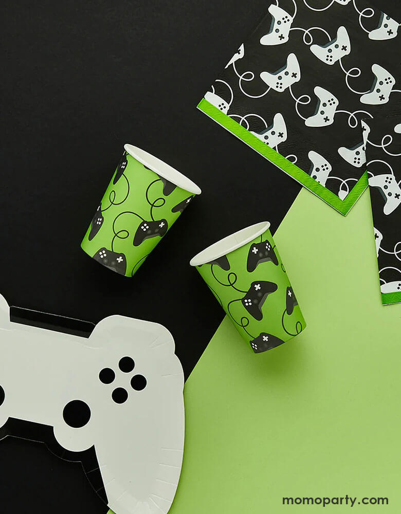 A video game themed party collection from Momo Party by Hooty Balloo including a white video game controller shaped paper plate, two green video game controller motif party cups, and two black game controller motif large napkins with green edge, all on a classic black and green color blocked background, perfect for any game events or a kid's video game themed birthday party.