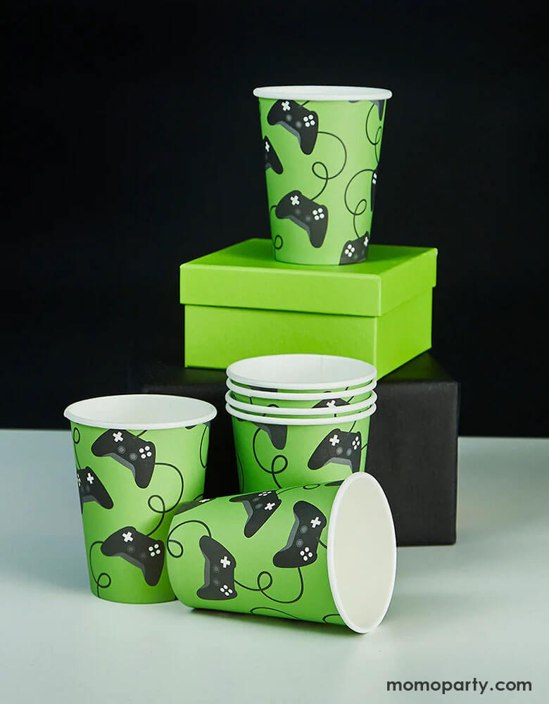 Momo Party's 7.4 oz Game Controller Party Cups by Hooty Balloo stacked on top of two gift boxes in black and green. These black and green paper cups are perfect for gamers and video game enthusiasts.