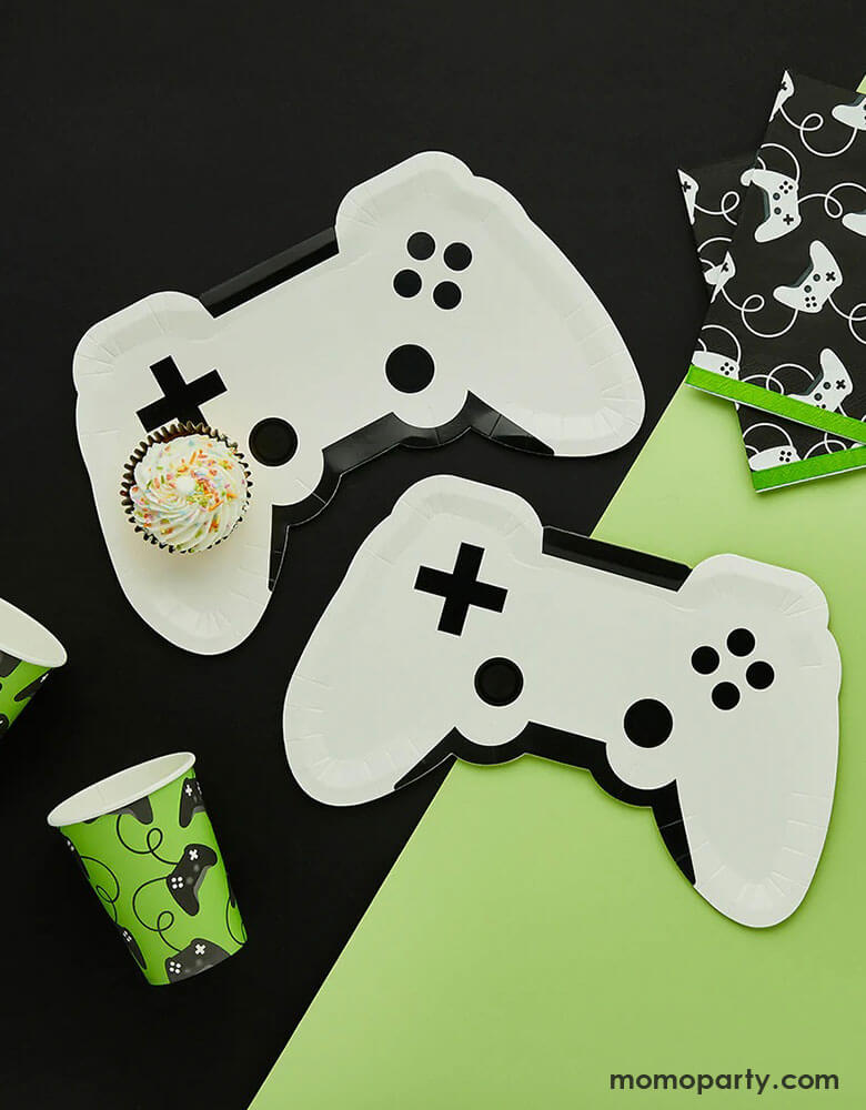 A video game themed party collection from Momo Party by Hooty Balloo including two white video game controller shaped paper plates, two green video game controller motif party cups, and two black game controller motif large napkins with green edge, all on a classic black and green color blocked background, perfect for any game events or a kid's video game themed birthday party.