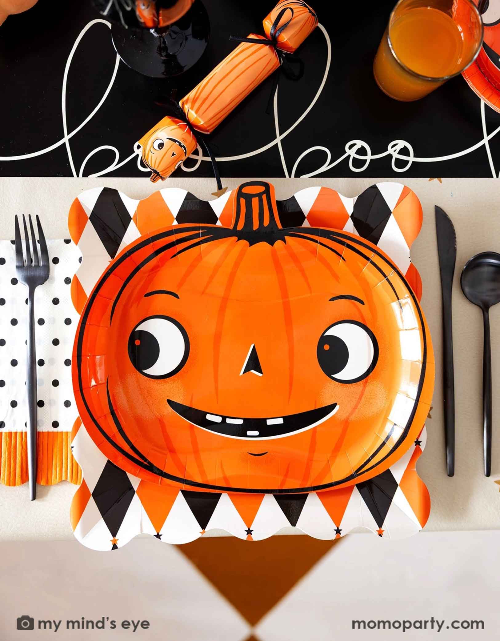 A festive vintage Halloween themed party table setting featuring multiple vintage Halloween themed party supplies from Momo Party including the orange and black harlequin plate, a vintage Halloween pumpkin shaped plate, the polka dot orange fringe dinner napkin, pumpkin party crackers on the boo paper table runner. With drinks and black cutlery set, this fun tablescape is perfect for a kid's friendly Halloween celebration. 