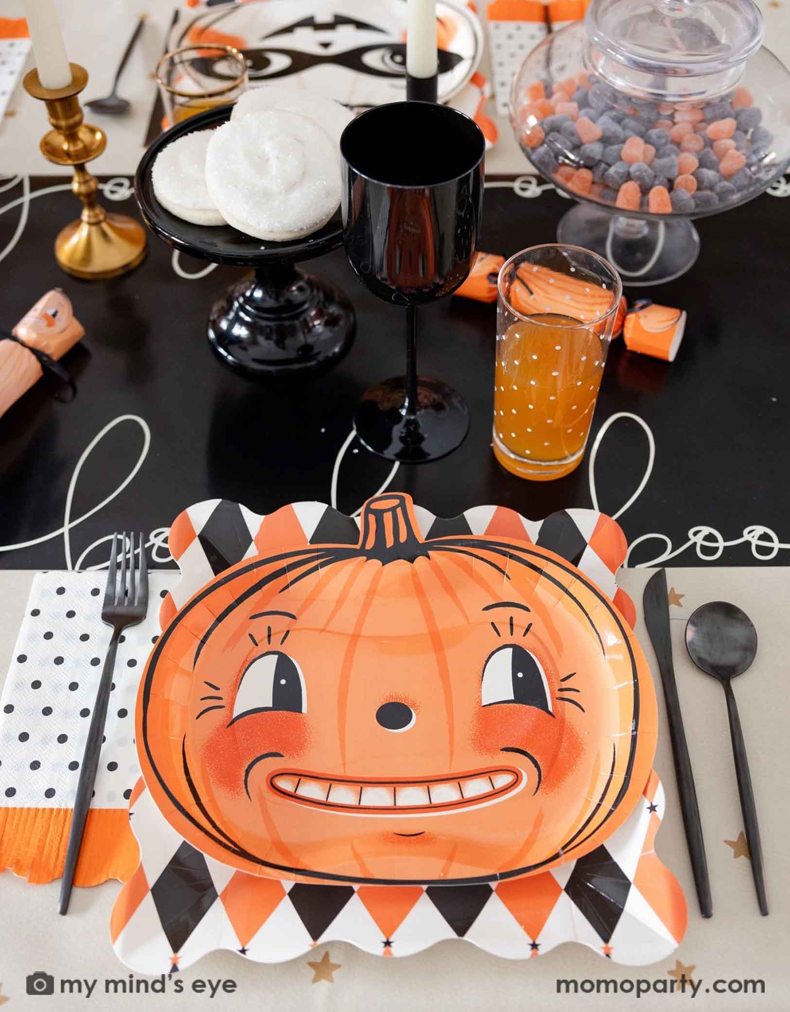 A festive vintage Halloween themed party table setting featuring multiple vintage Halloween themed party supplies from Momo Party including the orange and black harlequin plates, the vintage Halloween pumpkin shaped plates, the polka dot orange fringe dinner napkins, pumpkin party crackers on the boo paper table runner. With drinks, treats, candies and black cutlery set, this fun tablescape is perfect for a kid's friendly Halloween celebration. 