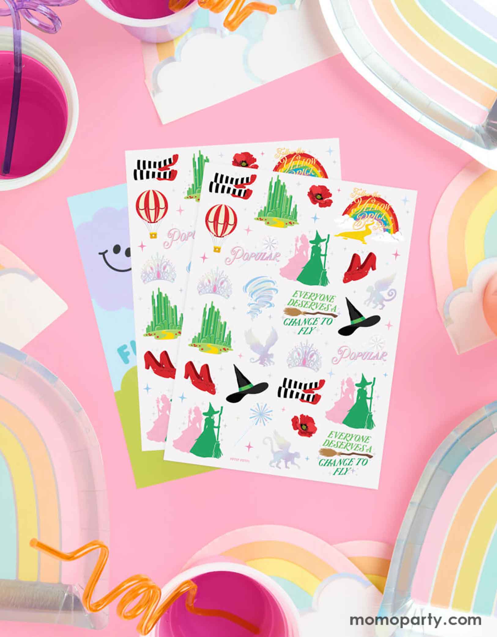 Momo Party's Emerald City Wicked Witch Temporary Tattoos by Xo, Fetti. Featuring  green witch hats, broomsticks, and magical icons inspired by the Wizard of Oz. On the table around the tattoo sheets there are some rainbow shaped plates and party cups with pink juice, making it perfect for a Wicked themed birthday party celebration!