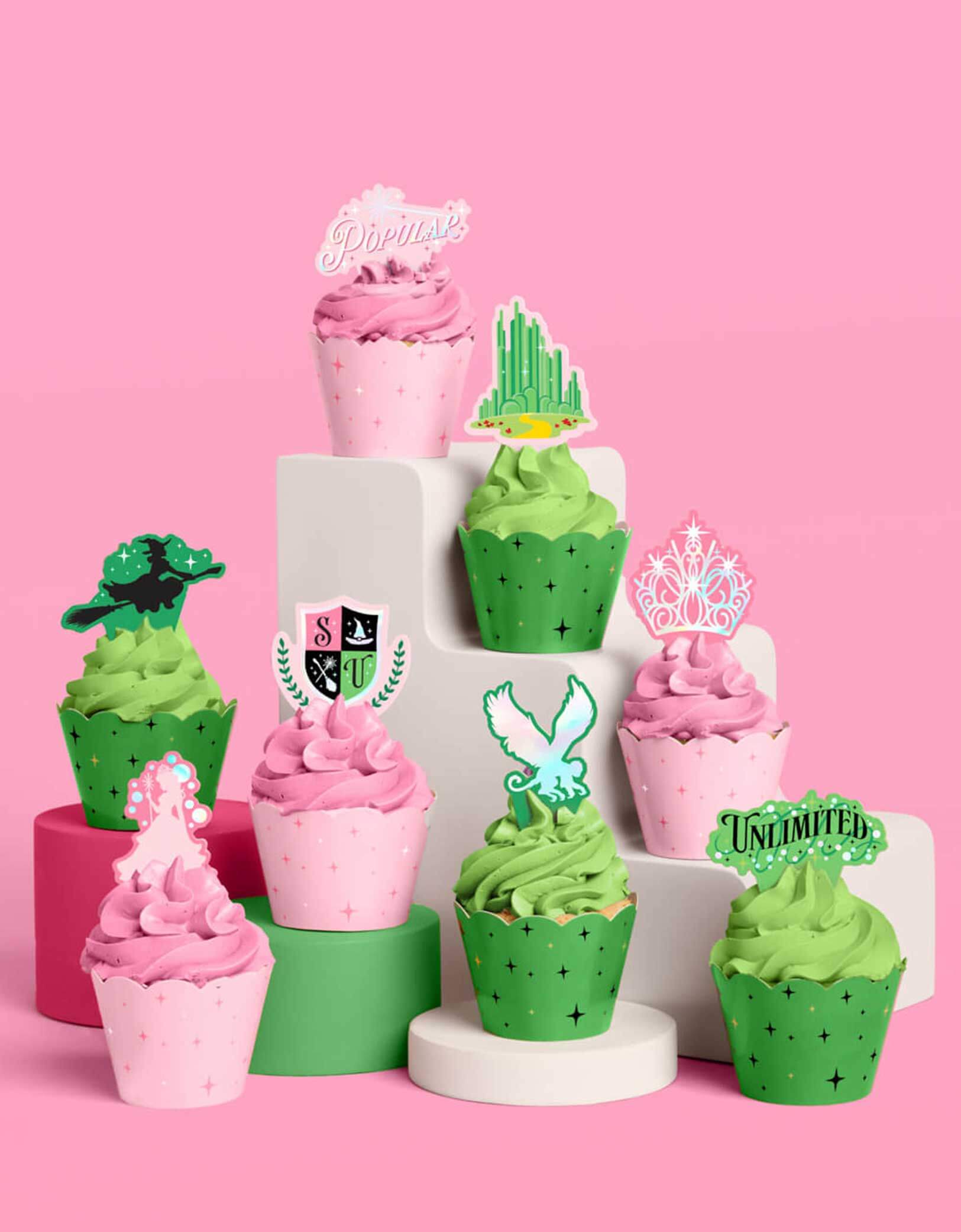 Wicked themed decorative cupcakes in green and pink with green and pink toppers and cupcake liners from Momo Party on a pink background.