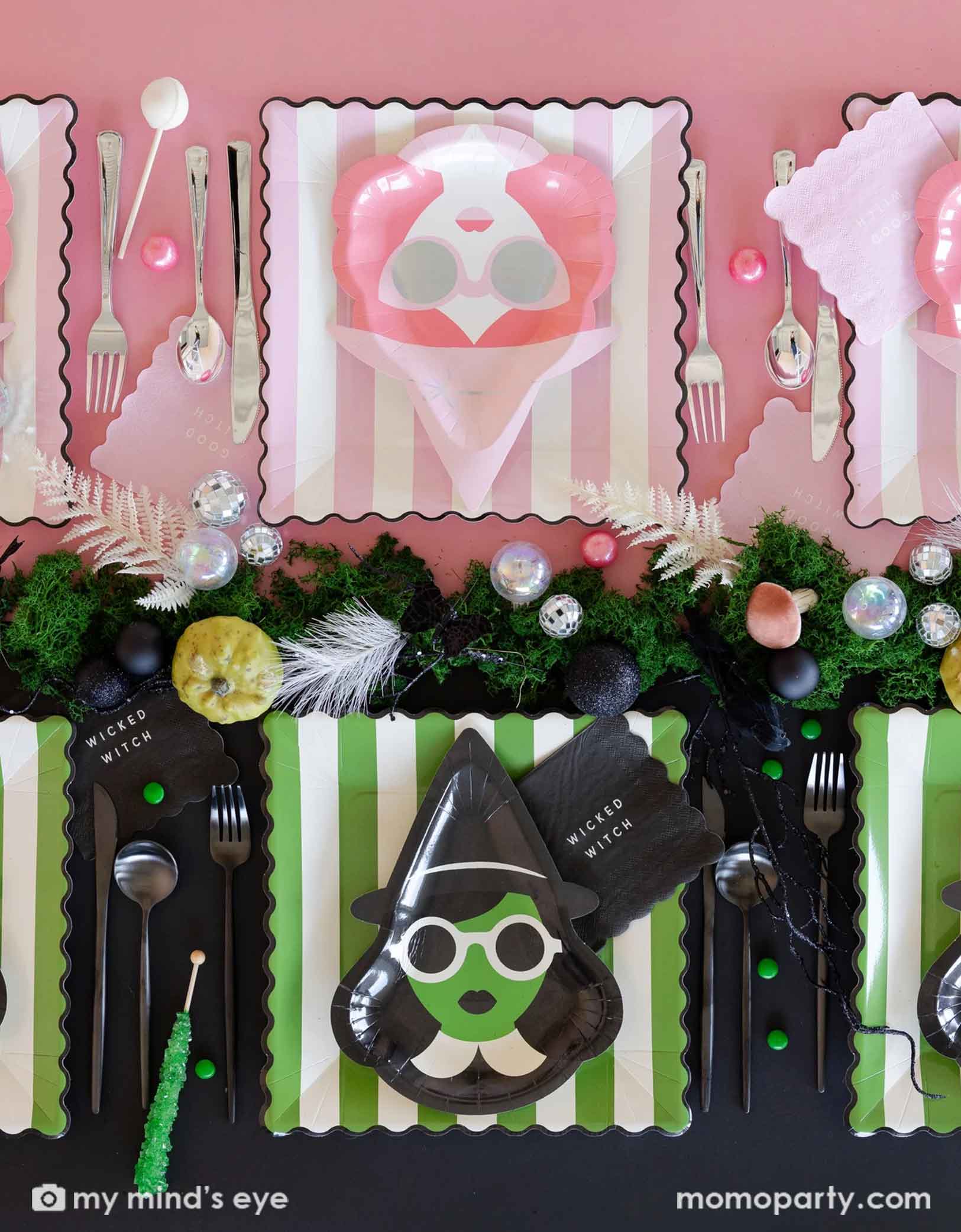 An overhead shot of a fun Wicked themed Halloween party table featuring Wicked witch themed green and pink party supplies from Momo Party on each side including with witch shaped plates, striped dinner plates, good witch wicked witch napkins, spoons, forks, and a table of treats and decorative disco balls on the table as centerpiece.