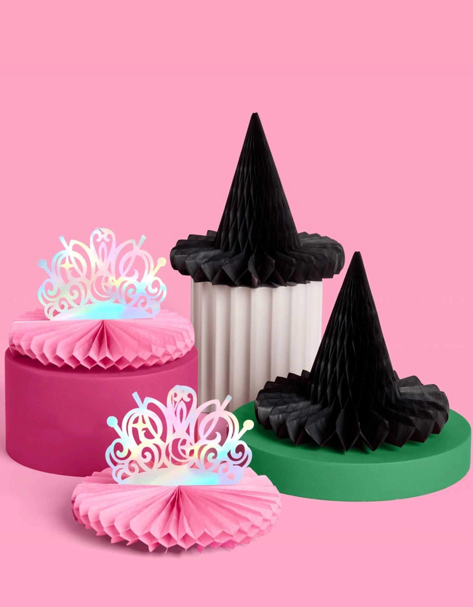 Momo Party's Wicked Pink Tiara & Black Witch Hat Honeycombs on a pink background. Featuring whimsical designs inspired by Glinda’s sparkle and Elphaba’s iconic style, these decorations add a magical touch perfect for fans of the beloved Wicked musical. Easy to unfold and display, they create an enchanting atmosphere that will make your celebration truly spellbinding.