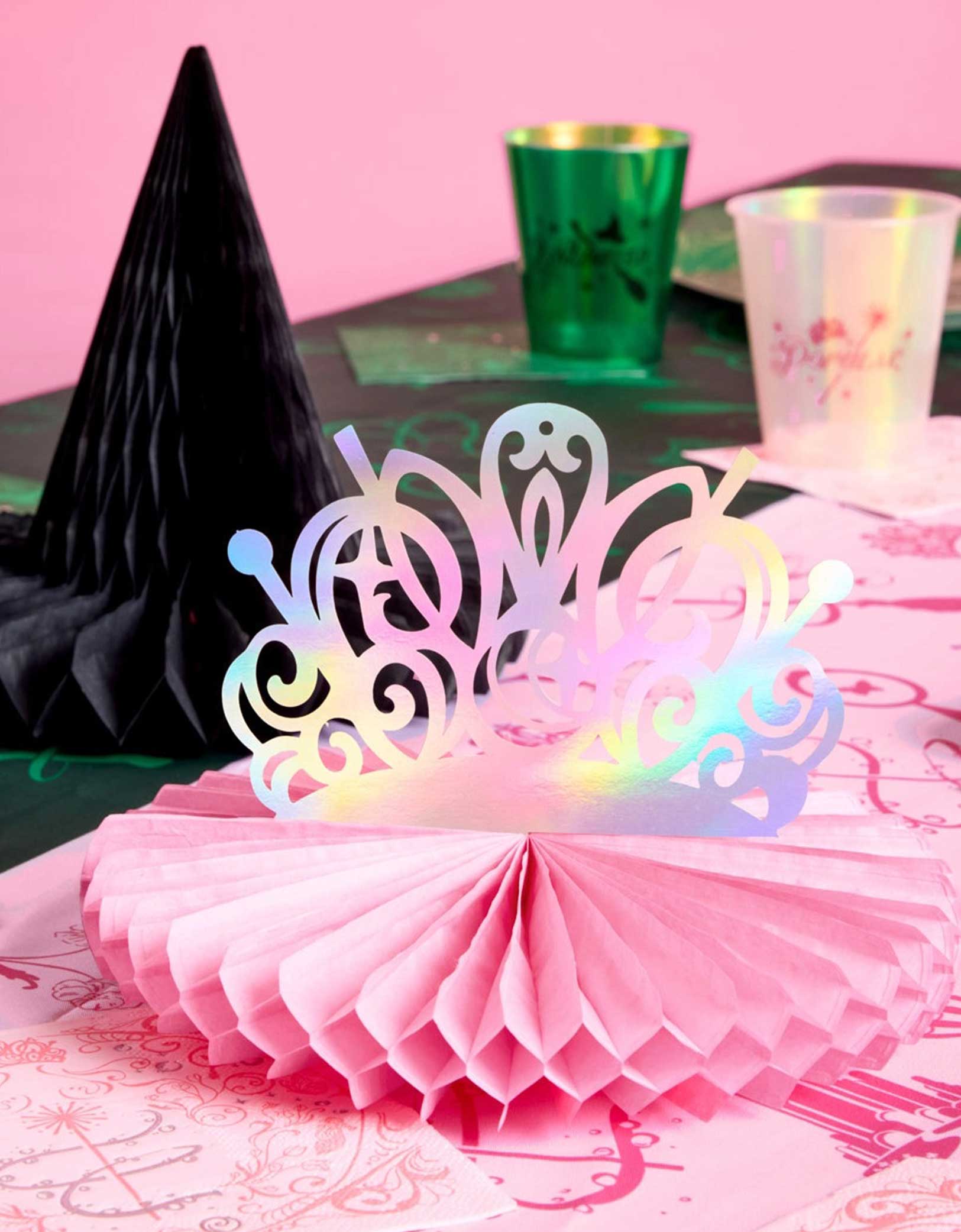 A festive Wicked themed party table featuring various of Wicked themed tablewares and decorations from Momo Party including Wicked Tiara & Witch Hat Honeycomb Set, Wicked party cups in green and green and Wicked party plates, napkins in green and pink on a Wicked themed tablecloth.