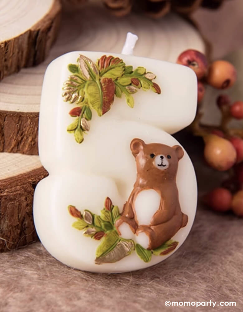 An adorable woodland themed kid's number five birthday candle a cute bear design and some foliage from Momo Party on a table with decorative wood logs and berries, filled with autumn and fall vibes. This charming candle is perfect for kid's woodland themed second birthday party celebration.