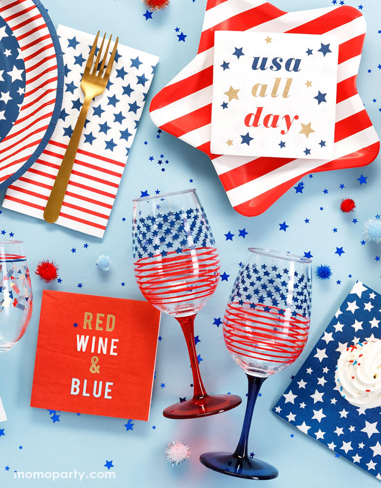 4th of July party table filled with CR Gibson Signature Americana Striped Star Plates, Americana Small Napkins, Red wine & blue napkins, Americana Dinner Plate with Americana  Guest Lunch Napkins, cupcakes, americana glasses, and star shaped confetti.