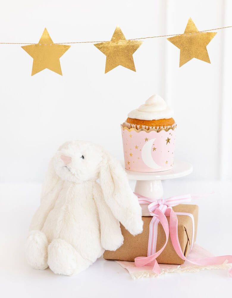 My Minds Eye Baby Pink 5 oz Food Cup with a cupcake next to a white stuffed bunny decoration with gold star party banner on the wall for a baby girl shower 