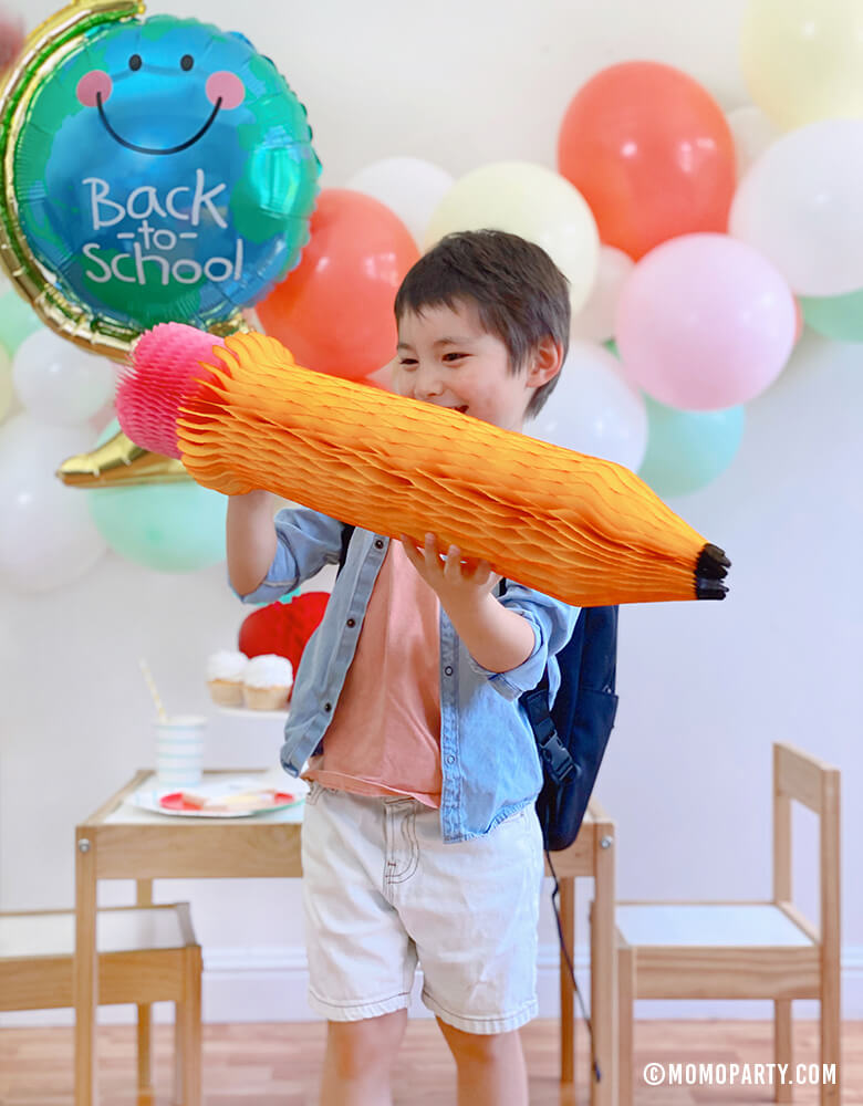 Boy holding a Devra Party 24" Back To School Pencil Shaped Honeycomb Decoration at his Back to School party, a 2020 Quarantine back to school home Party, modern Back to school party celebration.