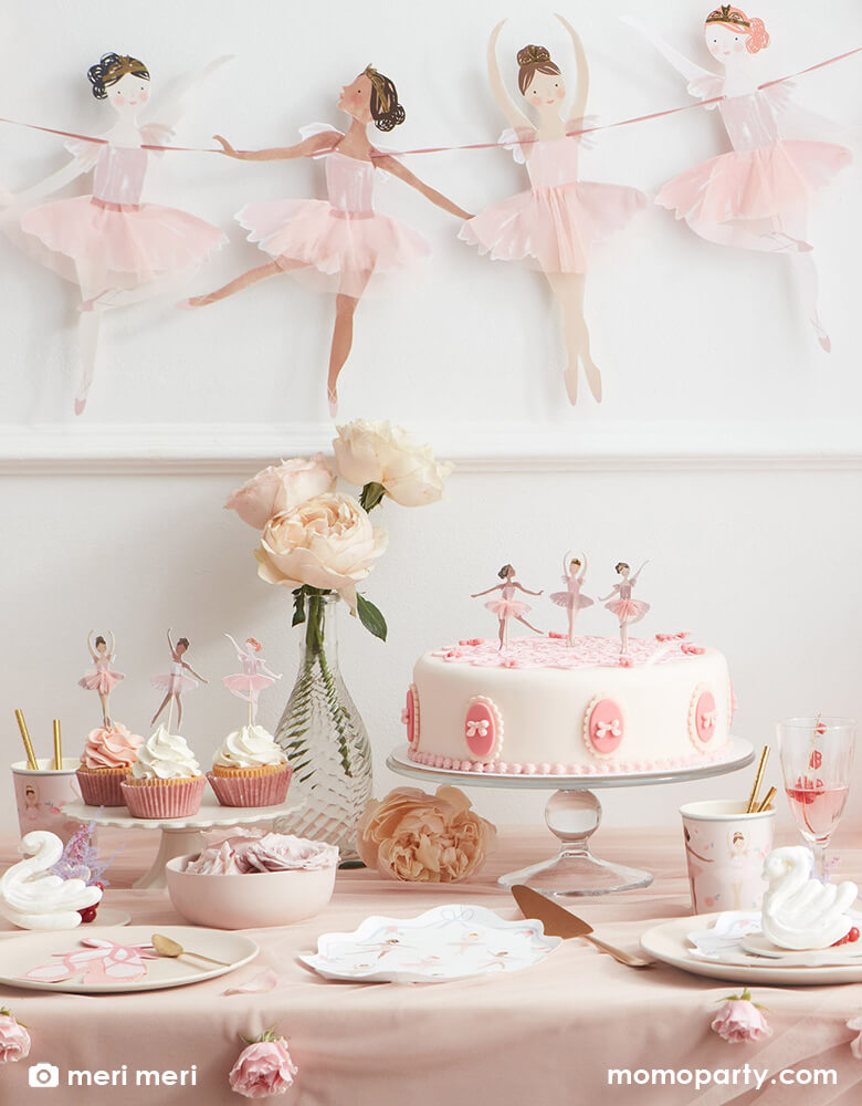 Ballet themed birthday party table decorated with Ballerina Plates from merimeri, Ballet Slippers Napkins in a plate, Ballet paper Cups with gold straws, cupcakes decorated with Ballerina cupcake toppers from Ballerina Cupcake kit, fresh flowers in a vese, swan decorations, all on a pink and flesh toned silk tablecloth. and Ballerina Garland on the wall. These Beautiful and modern designed party supplies are perfect for a Ballerina birthday party, girl birthday party, princess party, nutcracker themed party