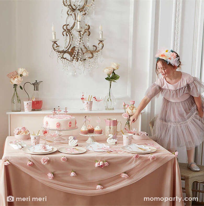 Ballet themed birthday party table setting allet themed birthday party table setting with a little girl in a lace dress and ballet shoes standing on a chair pointing to a plate full of Ballerina Plates from merimeri, Ballet Slippers Napkins, tissues, Ballet paper Cups, cupcakes and cupcakes with cupcake toppers from Ballerina Cupcake kit, flowers, swan decorations, all on a pink and flesh toned silk tablecloth. Such a modern and dreamy ballet themed birthday party 