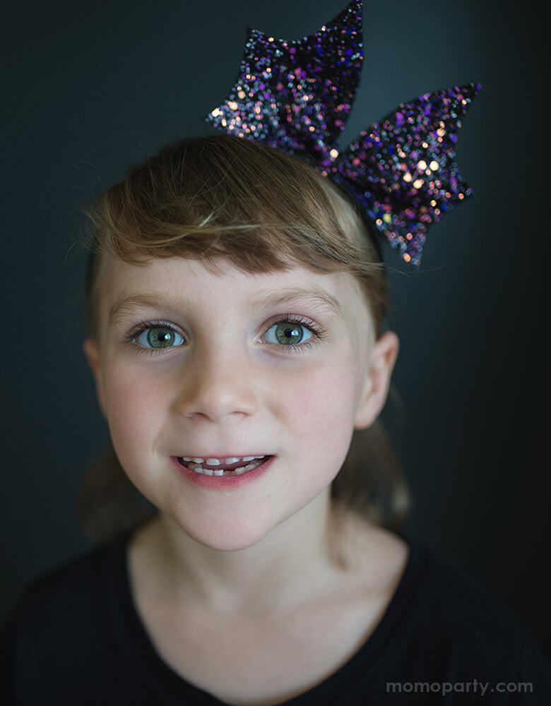 Girl wearing Great Pretenders - Bat Bow Headband. This sparkly bat bow headband in purple color will add an extra Halloween flair to any outfit! Beautiful and affordable Accessory for girl, Accessory for kid sold by party boutique online store momoparty.com
