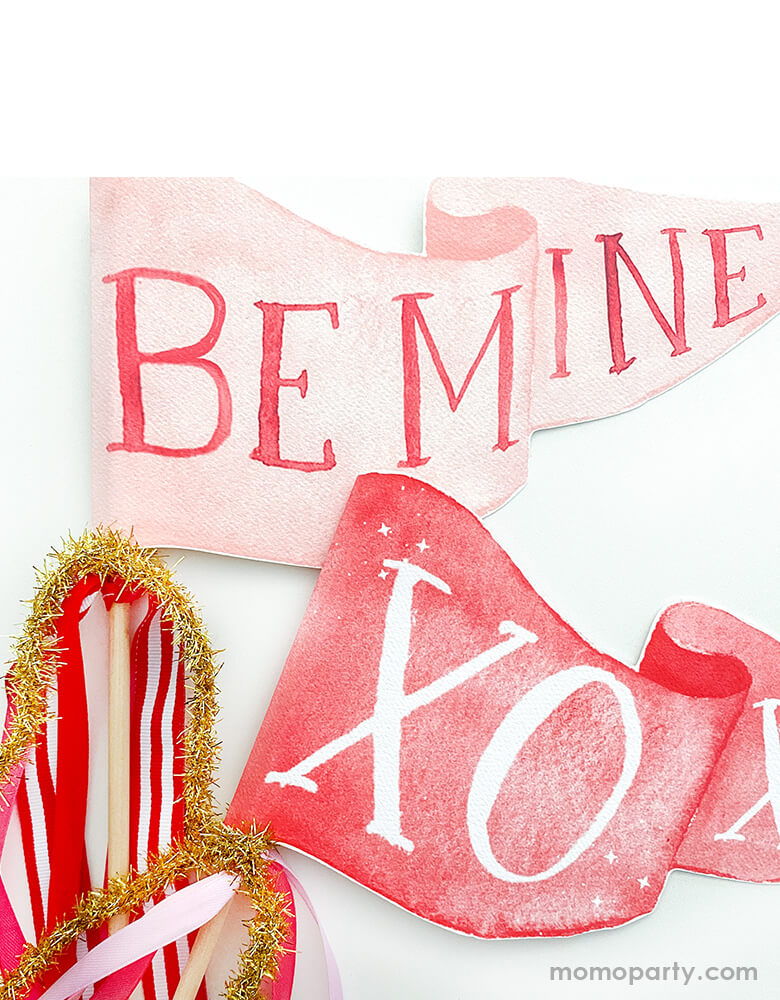 Close up details of Cami Monet - Be Mine Party Pennant and XOXO party pennant. This Handmade pennant made in United States of America, in Size: 10 x 5 inches. This is made of 120 lb. luxe watercolor texture paper with handwriting "Be Mine" and "xoxo" text in watercolor illustration for extra whimsy. With matched red pink and gold mixed Ribbon and sparkle garland. These adorable party pennants are perfect for a sweet Valentine's Day celebration!