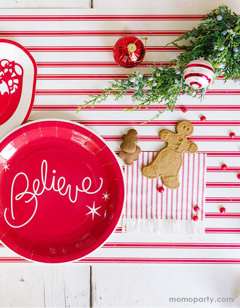 Classic christmas party table decorated with My Minds Eye BELIEVE 9" BELIEVE PLATE, and BELIEVE COCKTAIL NAPKIN. ginger bread cookies, ornament, on top of BELIEVE Red STRIPED TABLE RUNNER.