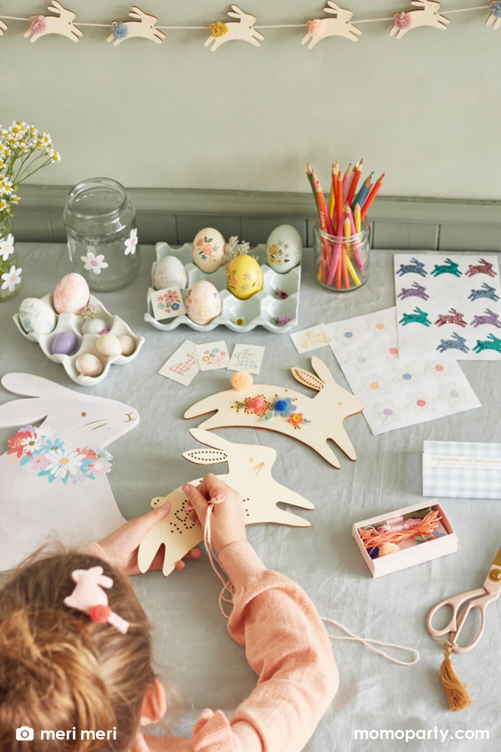 Kid playing Easter Activities on a table with Egg Decorating with tattoos, and bunny glitter stickers, Meri Meri Bunny Embroidery Kit. She is embroidering into  a Jumping Bunny shape plywood, It's a wonderful creative gift that is fun to make, and is then a fabulous decoration to hang up.