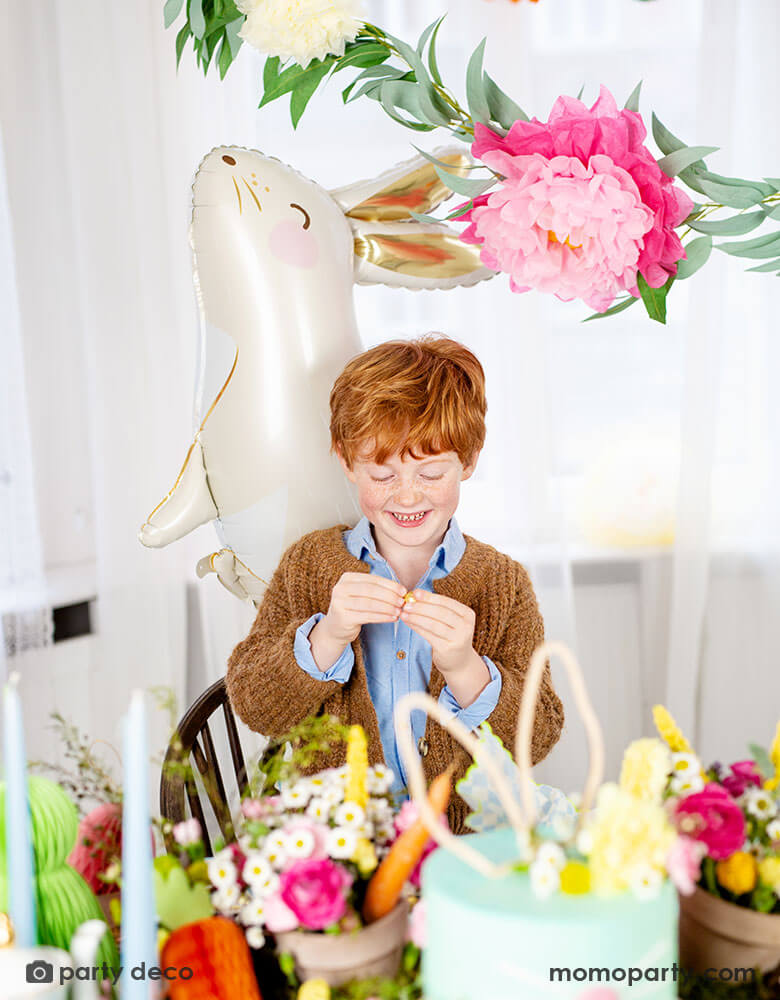 A beautiful Easter table decorated with spring flowers and honeycomb Easter egg, bunny and carrot decorations by Party Deco, with Momo Party's adorable 33 x 32" bunny shaped foil balloon by Party Deco in front of floral garland sets and tissue paper bunting garland, it makes a perfect inspiration for Easter celebration ideas with kids.
