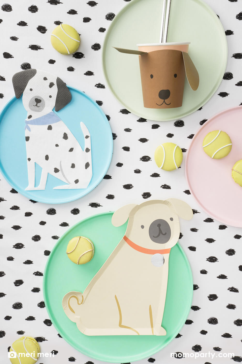 Momo Party kid's puppy dog themed birthday party table flat lay, decorated with Pug Plates on a mint round plate, Brown Puppy Cup with silver foil straws on pistachio colored plate, Puppy Napkins on the light blue round plate, tennis ball macarons all on the black dots tablecloth,  These modern and cute design party supplies from Meri Meri of Cat and Dog Collection,will make an Insta-perfect party table for your kid's puppy or dog themed birthday party.