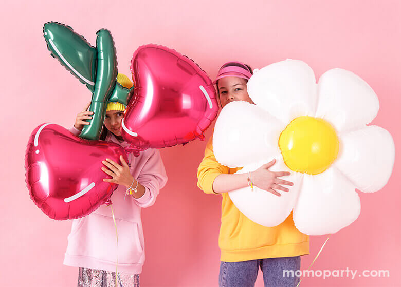 Two girls hugging Cherry Foil Balloon and Daisy Foil Mylar Balloon by Party Deco, in front of pink wall. these fun shaped balloons so bright the summer celebrations
