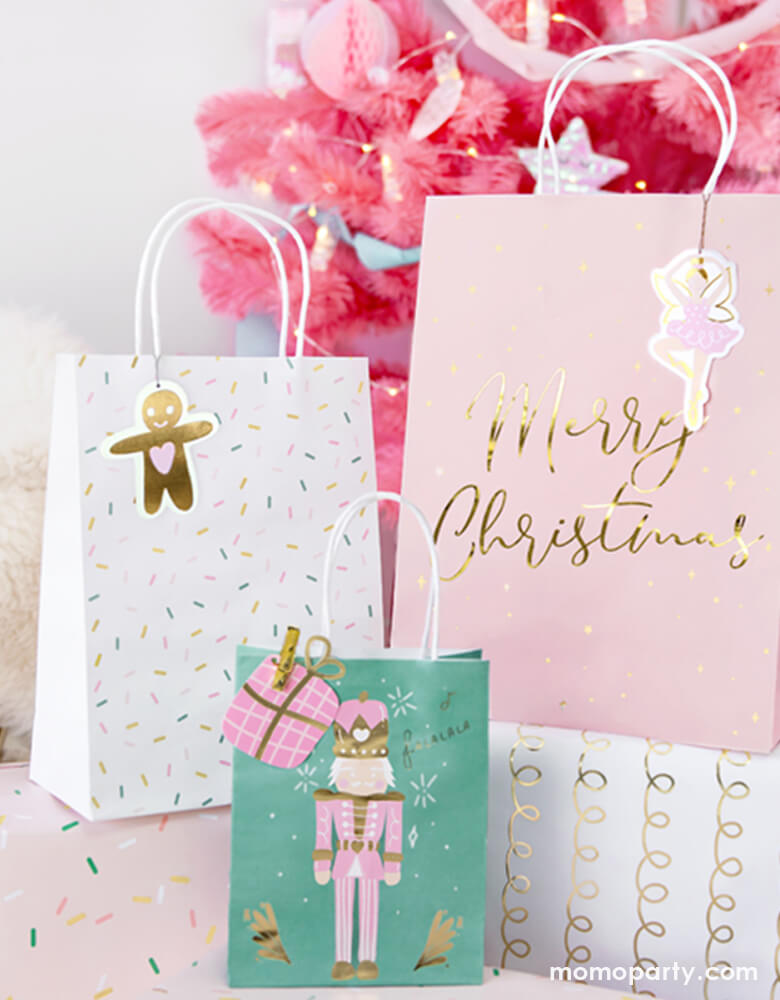 Closet up details of Party Deco Christmas Gift Bags and gift boxes under the Pink Christmas tree. These 3 designs party bags with gift bag shaped gift tag on the pink nutcracker illustrated green bag, gingerbread man gift tag on the sprinkles white bag, and pink ballerina gift tag  on the Pink bag with gold foil Merry Christmas sign. 