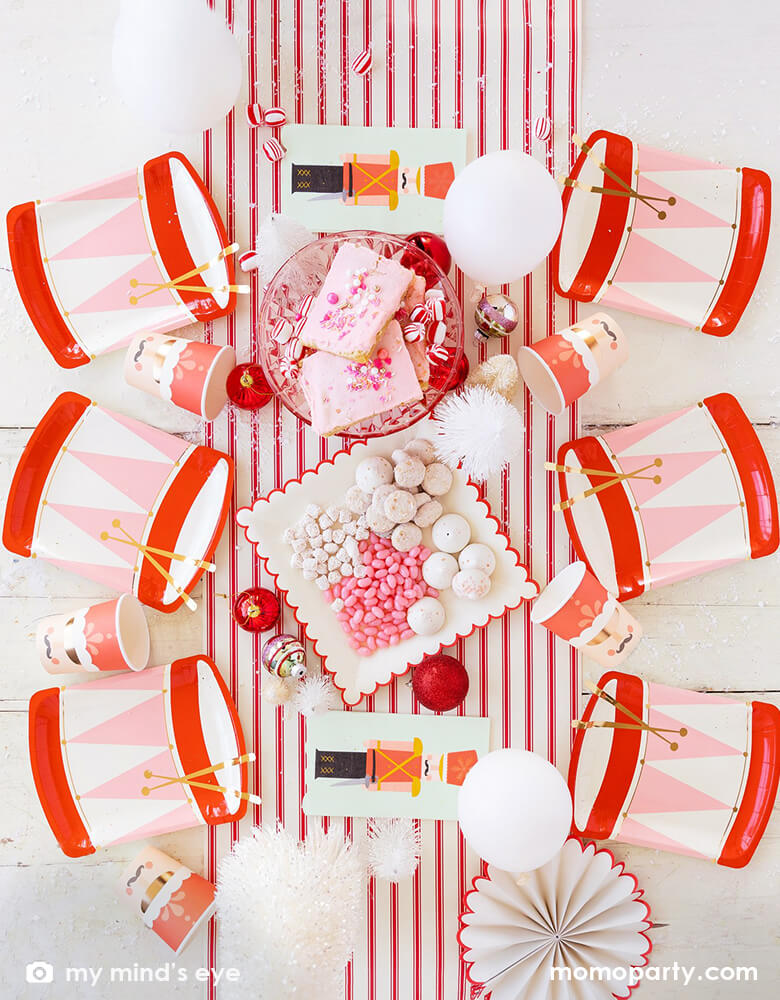 Holiday Christmas Family Table top view with Six My Mind's Eye Nutcracker Drum Shaped Plates, Nutcracker Napkins and Nutcracker Soldier Cups, sweets, cookies, ornaments, balloons and paper fan as center piece in the middle of the table over the Believe Christmas Red Striped Table Runner. These Morden and high quality party supplies with cute design in pink and red tone are so unique and adorable for holiday family gathering with kids and friends. Holiday partyware, party supplies at momoparty.com