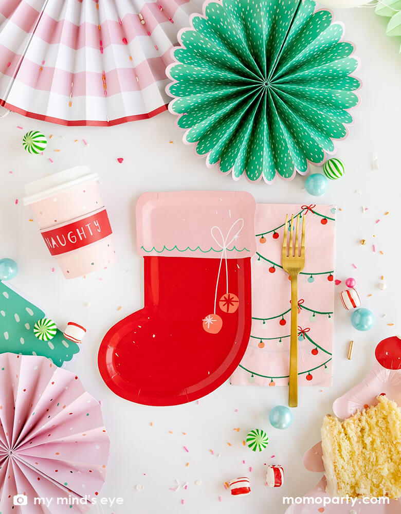 Modern fun Holiday Christmas Table decoration idea with Christmas Stocking Shaped Plates, Naughty or Nice Christmas Cozy To-Go Cups, String of Lights Guest Towel Napkins with gold folk on top, Oui-Party-Fa La La Christmas Paper Fans as centerpiece, cake on the pink christmas tree plate, and peppermint candies around these modern tablewares.
